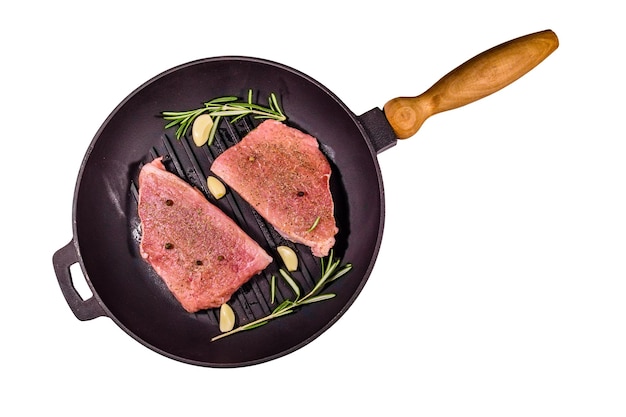 Rohe Steaks mit Knoblauch, Rosmarin und Gewürzen in einer gusseisernen Grillpfanne isoliert auf weißem Hintergrund