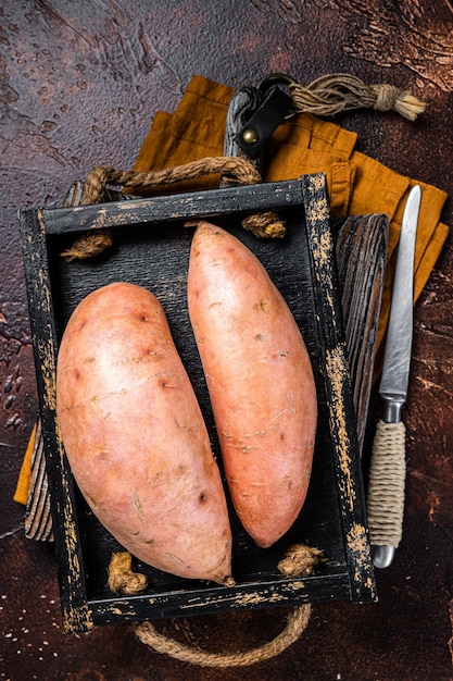 Rohe Süßkartoffeln in einem Holztablett frische Batata Dunkler Hintergrund Ansicht von oben