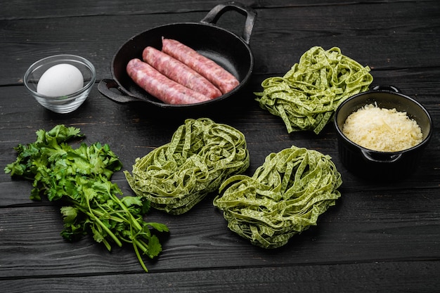 Rohe Tagliatelle-Würstchen-Zutaten, auf schwarzem Holztischhintergrund