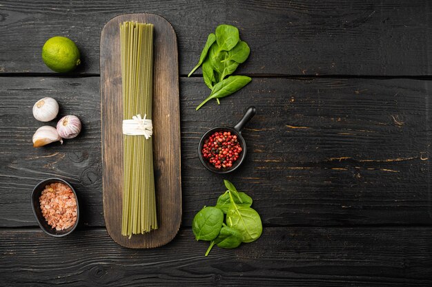 Rohe trockene grüne Spaghetti mit Spinat-Set, auf schwarzem Holztischhintergrund, Draufsicht flach, mit Kopierraum für Text