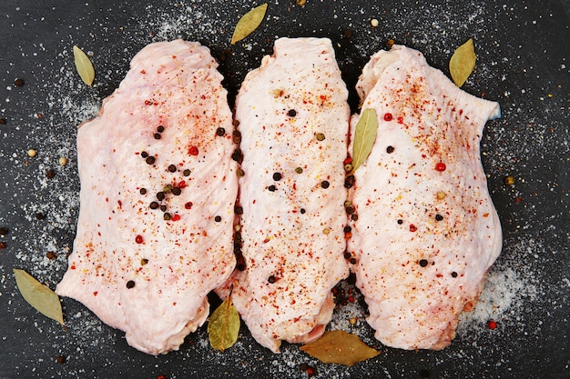 Rohe truthahnflügel mit gewürzen auf schwarzem schiefertablett. frische puten wingette mit einer mischung aus paprika auf einem schwarzen steintablett