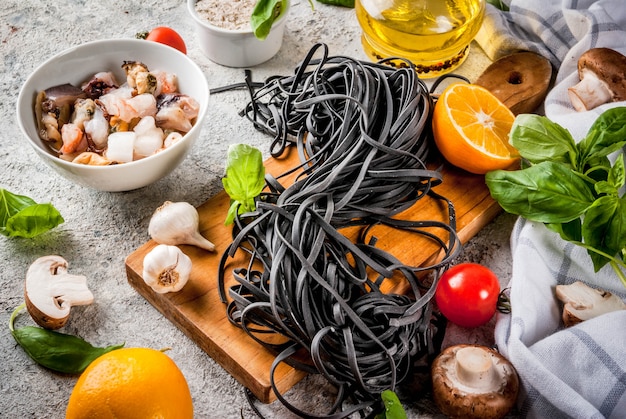 Rohe ungekochte schwarze Kopffüßertintenspaghettis mit Bestandteilen für das Kochen des Abendessens