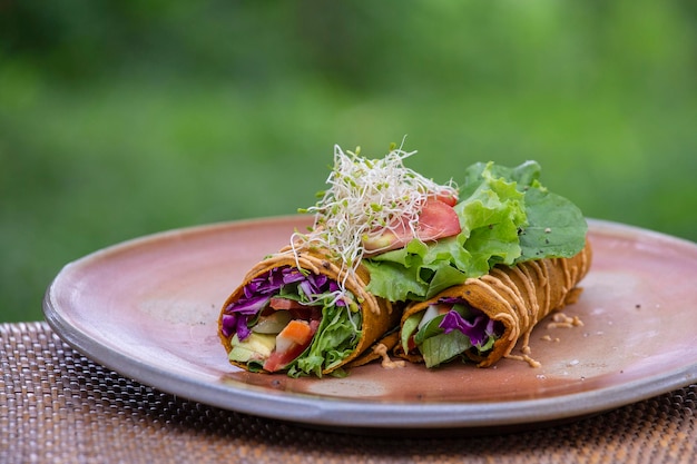 Rohe vegane Karotten- und Kreuzkümmel-Wrap-Rolle, gefüllt mit zerkleinertem Salat, Tomaten, Avocado, Spinat und wohlschmeckendem Zucchini-Hummus Gesunde Sommerkost Nahaufnahme zwei Rollen in der Platte