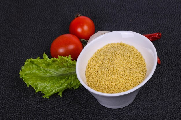 Roher Couscous in der Schüssel serviert Salatblätter Tomaten und Pfeffer