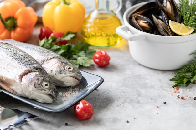 roher Dorado-Fisch mit Gewürzen, Zitrone und Petersilie in einer schwarzen Grillpfanne auf weißem Beton