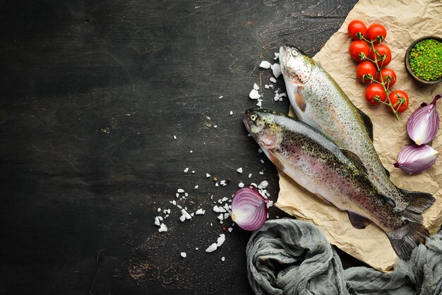 Roher Fisch mit Gemüse auf schwarzem Holzhintergrund Fischforelle Draufsicht Freier Platz für Ihren Text