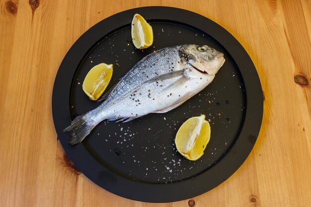 Roher frischer Fischdorado mit Zitrone und Gewürzen auf einem Holztisch