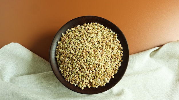 Roher grüner Buchweizen in einer braunen Tonplatte auf braunem Hintergrund. Veganes Bio-Lebensmittelkonzept.