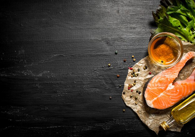 Roher Lachs mit Olivenöl, Gewürzen und Kräutern an schwarzer Tafel.