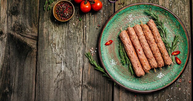 Roher Lula-Kebab am Spieß mit Gewürzen auf hölzernem Hintergrund der Platte. Langes Bannerformat. Ansicht von oben