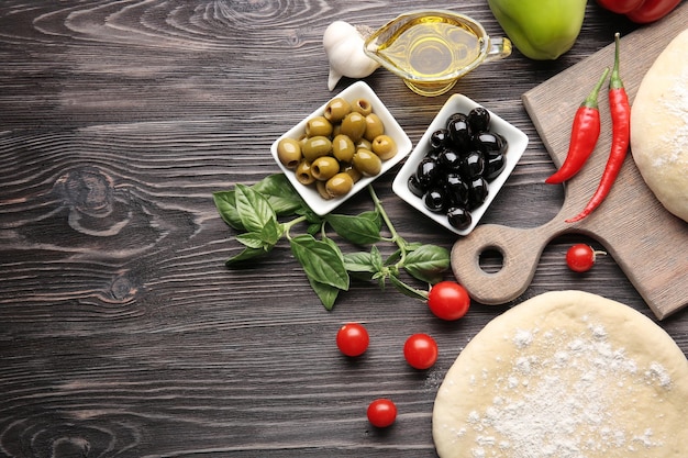 Foto roher pizzateig mit bestandteilen auf holztisch