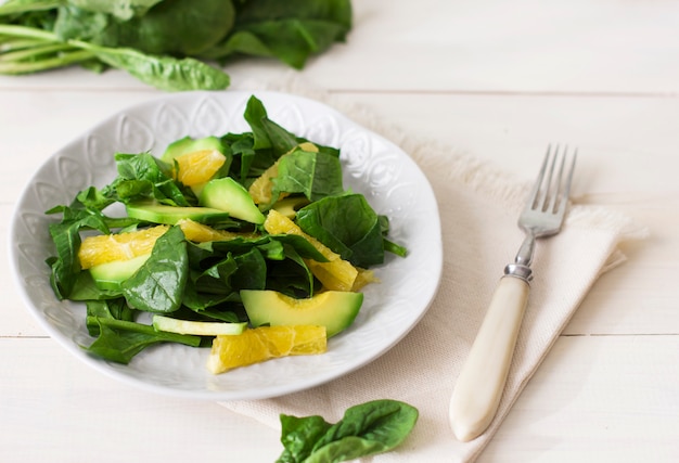 Roher Salat von Spinat, Avocado und Orange auf einem weißen hölzernen Hintergrund