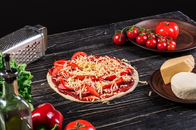 Roher Teig für die Pizzazubereitung mit Zutaten: Tomatensauce, Mozzarella, Tomaten, Basilikum, Olivenöl, Käse, Gewürze, serviert auf rustikalem Holztisch. Flacher Lay-Stil. Italienische Pizza.