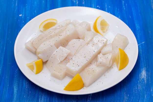 Roher Tintenfisch mit Pfeffer und frischer Zitrone auf weißem Teller