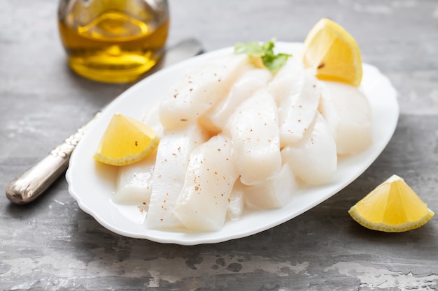 Roher Tintenfisch mit Pfeffer und frischer Zitrone auf weißem Teller