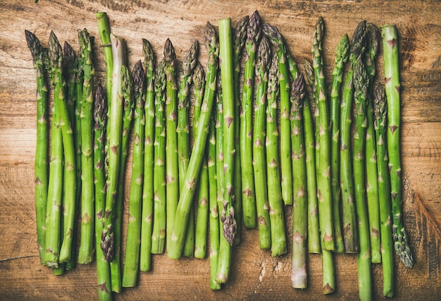 Roher ungekochter grüner Spargel in Reihe über Holzhintergrund