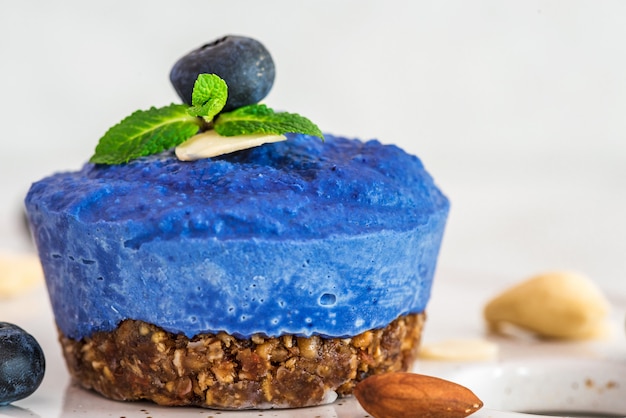 Roher veganer Kuchen der Heidelbeer-, Acai- und Schmetterlingserbsenblume mit frischen Beeren, Minze, Nüssen. gesundes veganes Lebensmittelkonzept