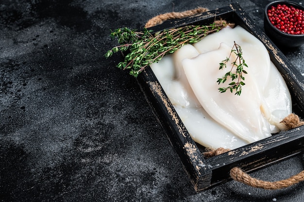 Roher weißer Tintenfisch oder Calamari in einem Holztablett mit Kräutern