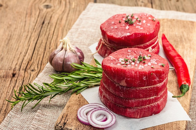 Rohes Auge eines runden Steaks mit Gewürzen und Kräutern auf hölzernem Hintergrund. Frisches Fleisch zum Kochen gesunder Lebensmittel, Kopierraum im rustikalen Stil