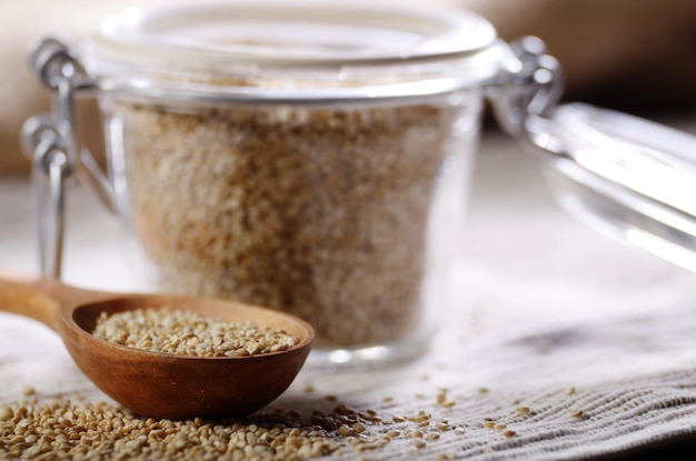 Rohes Bio-Superfood glutenfreie Quinoa-Samen in Holzlöffel und luftdichtem Glasglas auf dem Küchentisch in der Nähe