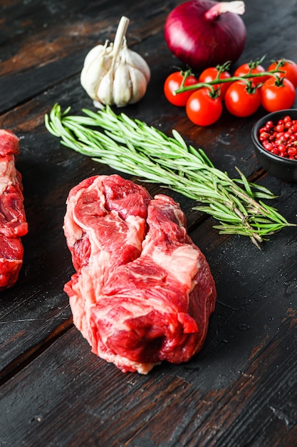 Rohes Chuck Eye Roll-Rindersteak, geschnitten mit rosmarinrotem Onin, Knoblauchpfefferkörnern und Tomaten auf altem dunklem Holztisch. Seitenansicht.