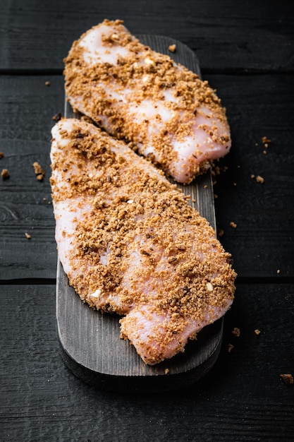 Foto rohes crumbet-hähnchenfilet mit zutaten auf schwarzem holzhintergrund