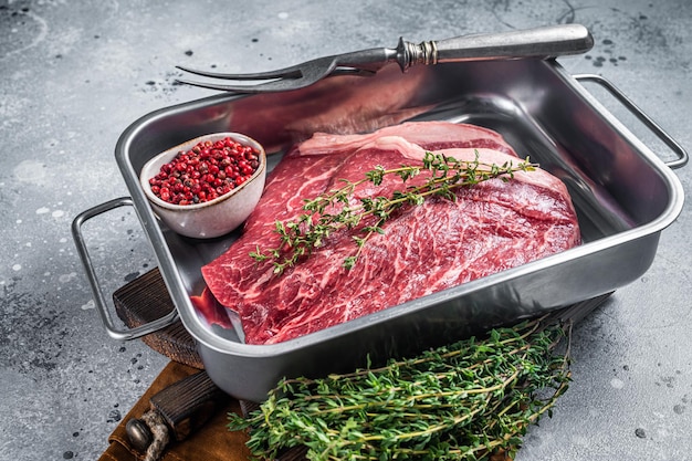 Rohes dünnes marmoriertes Rindersteak mit Gewürzen im Küchentablett. Grauer Hintergrund. Ansicht von oben.