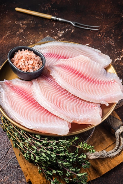 Rohes Fischfilet von Tilapia in einem Teller mit Gewürzen Dunkler Hintergrund Draufsicht