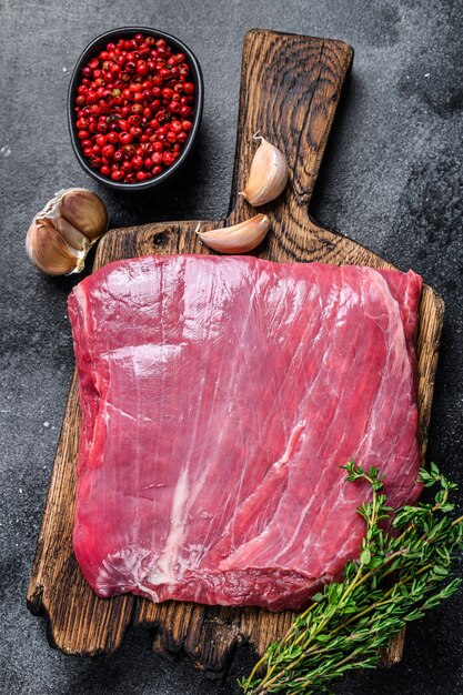 Rohes Flanken- oder Klappenrindfleischsteak auf einem hölzernen Schneidebrett. Schwarzer Hintergrund. Ansicht von oben.