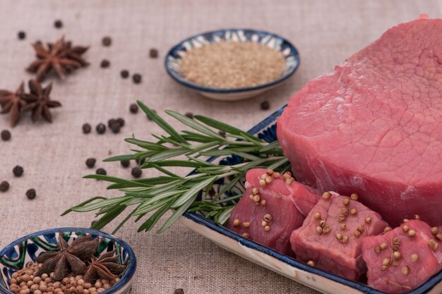 Rohes Fleisch mit Gewürzen und Kräutern in einem quadratischen Teller auf einem strukturierten Gewebe