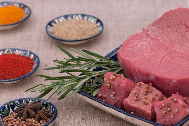 Rohes Fleisch mit Gewürzen und Kräutern in einem quadratischen Teller auf einem strukturierten Gewebe