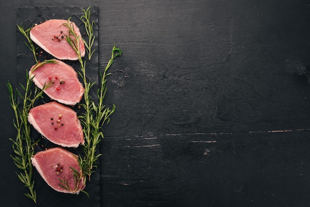 Rohes Fleisch Rindersteak mit Rosmarin und Gewürzen auf schwarzem Holzhintergrund Draufsicht Freier Platz für Text