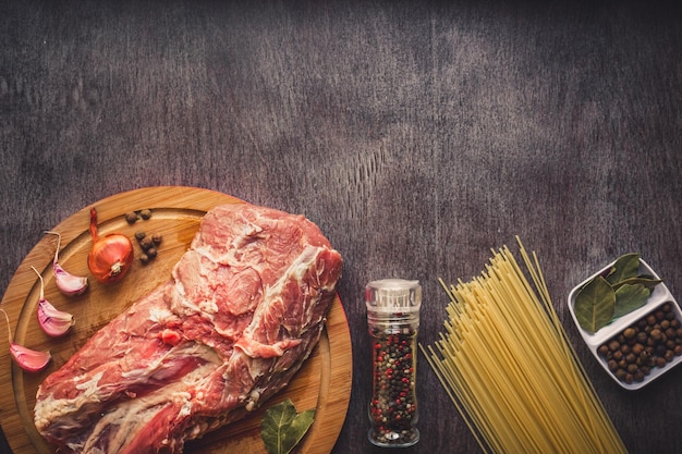 Rohes Fleisch Rindfleischscheiben auf einem Holzschneidebrett mit Spaghetti, Knoblauch, Gewürzen, Pfefferkörnern, Salz und Dill zum Kochen von Nudeln. Ansicht von oben. Platz kopieren. Stillleben. Flach liegen