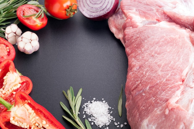 Rohes Fleischschweinefleisch mit Gewürzen und Gemüse auf einem dunklen Hintergrund