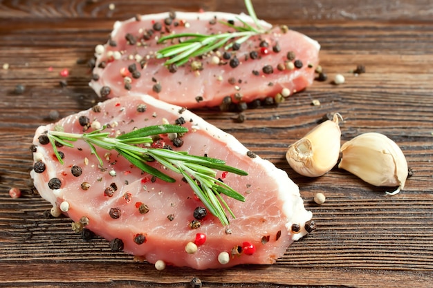 Rohes Fleischsteak mit Gewürzen auf braunem Holzbrett. Schweinefleisch, Rosmarin, Pfeffer, Gewürze und Knoblauch auf Holzuntergrund