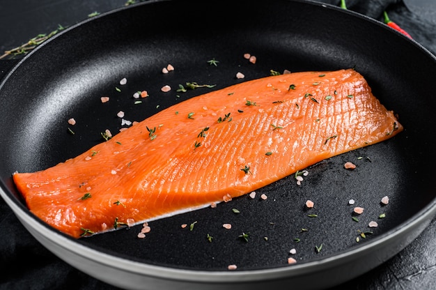 Rohes Forellenfilet mit Salz und Chili in einer Pfanne. Bio-Fisch. Schwarze Oberfläche. Draufsicht.