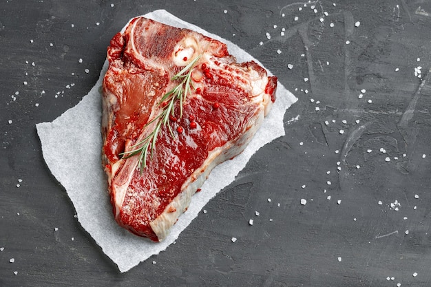 Rohes frisches Fleisch-T-Bone-Steak mit Gewürzen auf dunklem Hintergrund, Nahaufnahme