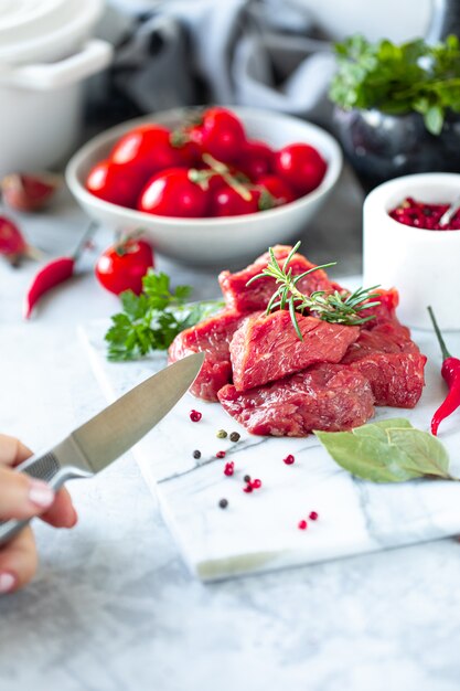 Rohes frisches marmoriertes Fleischsteak und und Fleischgabel auf weißem Marmorhintergrund. Messer in der Hand des Mannes