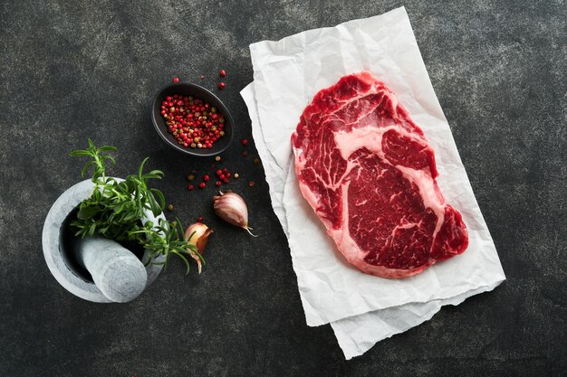 Rohes frisches Ribeye-Steak oder Ribeye-Steak Rohes frisches marmoriertes Fleisch Ribeye Black Angus und Gewürze Pfeffer Rosmarin Thymian und Salz auf altem rustikalem Holzhintergrund Draufsicht und Kopierbereich