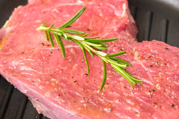 Rohes frisches Rindersteak mit Rosmarin auf einer Grillpfanne.