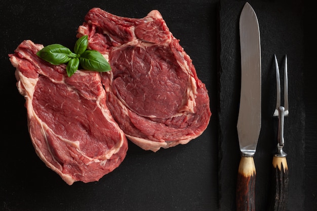 Rohes frisches Rindfleischsteak mit dem Knochen, den Gewürzen und den Gewürzen auf Steinschneidebrett.