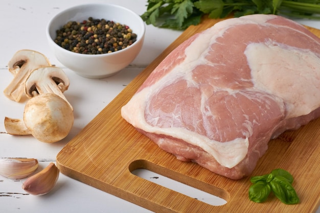 Rohes frisches Schweinefleisch Schinken Schweineschinken auf einem Schneidebrett gemischte Pfefferkörner Pilze Petersilie Knoblauch auf weißem Hintergrund