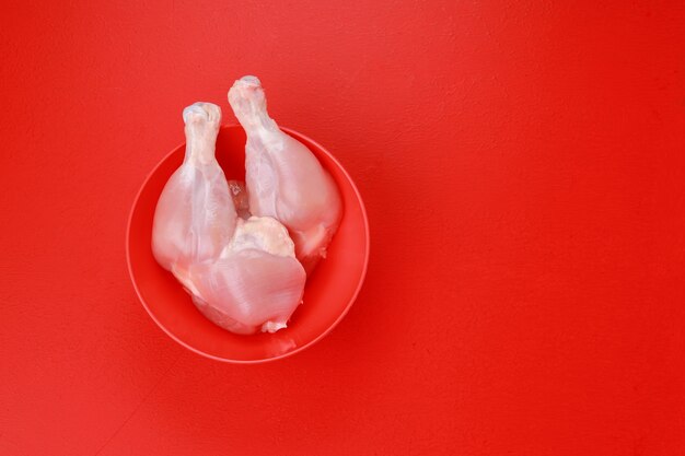 Rohes ganzes Hähnchenschenkel oder -schenkel ohne Haut in einer roten Schüssel auf einem roten einfarbigen Hintergrund angeordnet