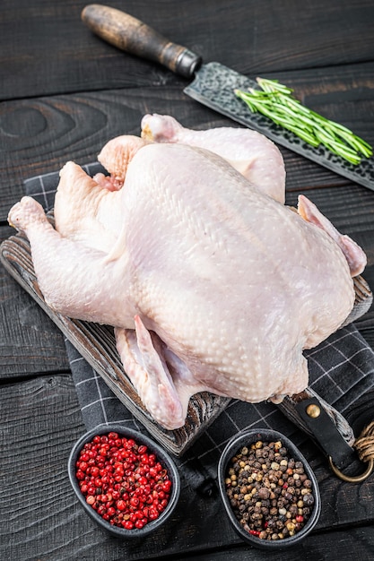 Rohes ganzes Huhn, Geflügelfleisch auf einem Holzbrett mit Kräutern. Schwarzer hölzerner Hintergrund. Ansicht von oben.