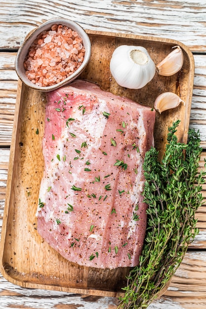 Rohes ganzes Schweinelendefleisch ohne Knochen mit Thymian und Salz auf rustikalem Brett. Weißer hölzerner Hintergrund. Ansicht von oben.