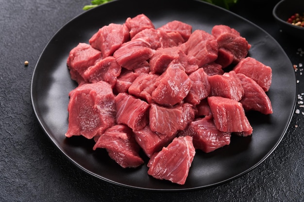 Rohes gehacktes rindfleisch rohes bio-fleisch rind- oder lammgewürze kräuter auf schwarzem teller auf dunkelgrauem betongrund gulasch rohes, ungekochtes fleisch fleisch mit blut draufsicht mit kopierbereich