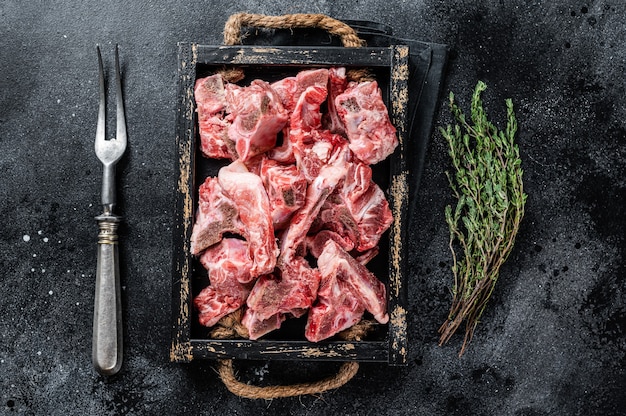 Rohes gewürfeltes Fleisch mit Knochen in einem Holztablett. Schwarzer Tisch. Draufsicht.