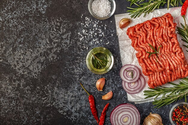 Rohes Hackfleisch auf Papier mit Zwiebeln, Kräutern und Gewürzen auf bla