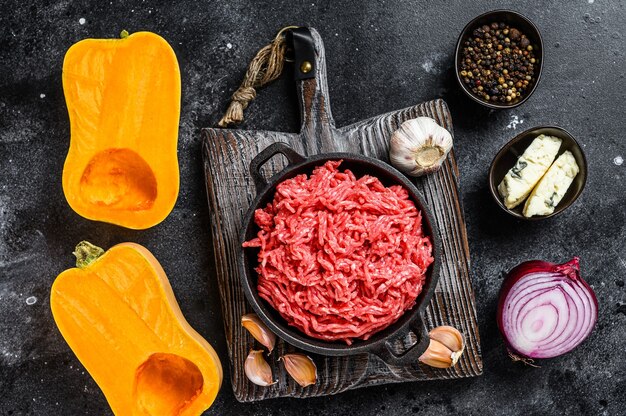 Rohes Hackfleisch, Kürbis mit Knoblauch und Zwiebeln. Schwarzer Hintergrund. Draufsicht.