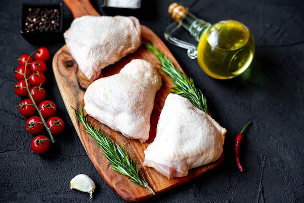 Rohes Hähnchen auf einem Schneidebrett mit Olivenöl und Tomaten